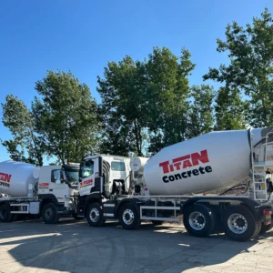 Two large white Titan Concrete concrete mixer trucks parked side-by-side in a construction yard under a clear blue sky.