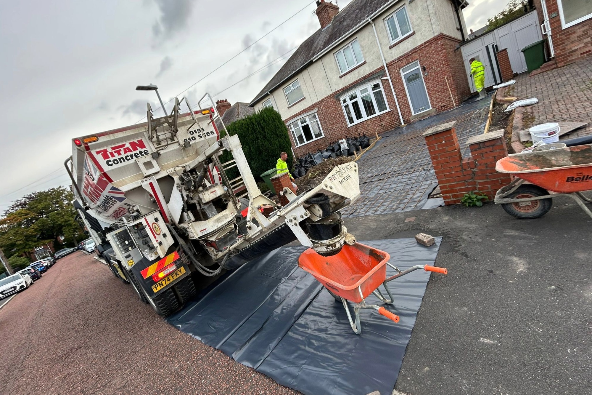 Titan Concrete truck outside of residential property pouring concrete into orange wheelbarrow, with two employees ready to lay concrete driveway.